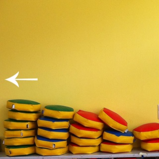 Struktur und Ordnung, sortierte Polster Struktur und Ordnung, gelbe Wand, Polster, kleine Kissen auf einer Bank liegend, mit weißem Zurückpfeil